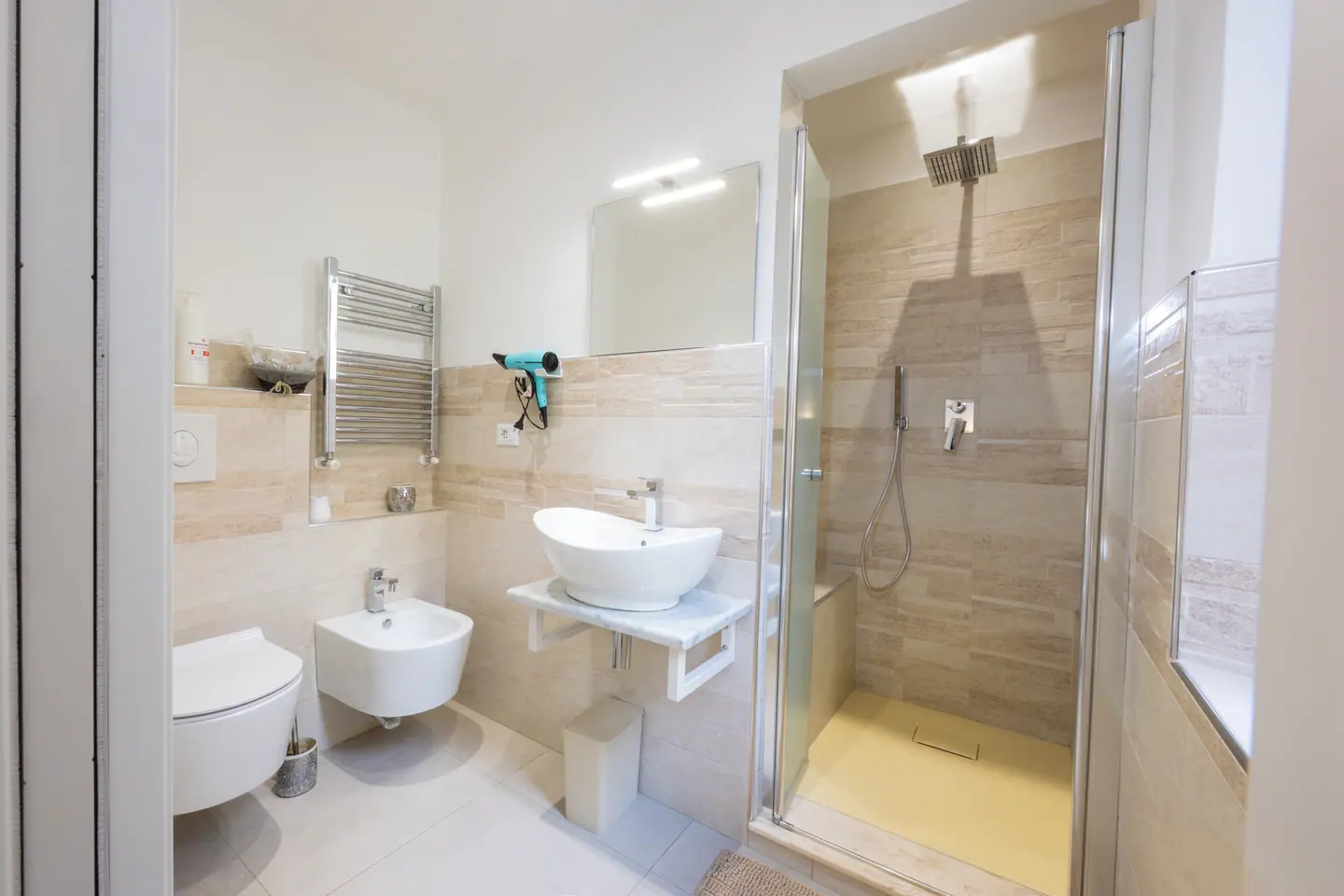 Il bagno privato in travertino, con lavabo ovale d'appoggio e doccia walk-in
