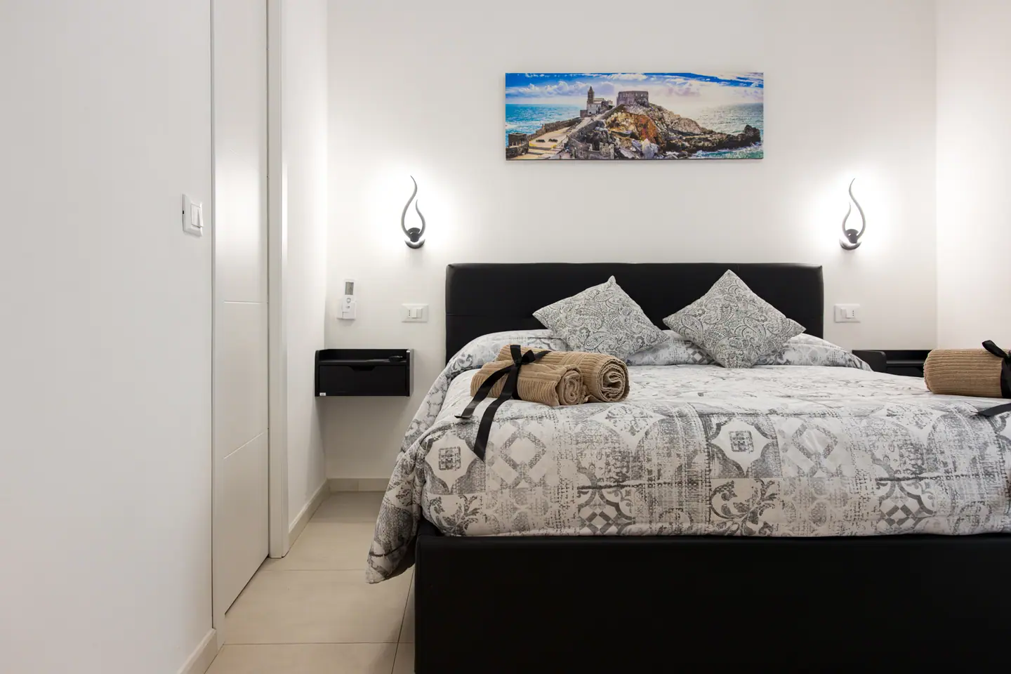 Letto in similpelle nera con applique a fiamma accese e stampa panoramica di Portovenere sopra la testiera